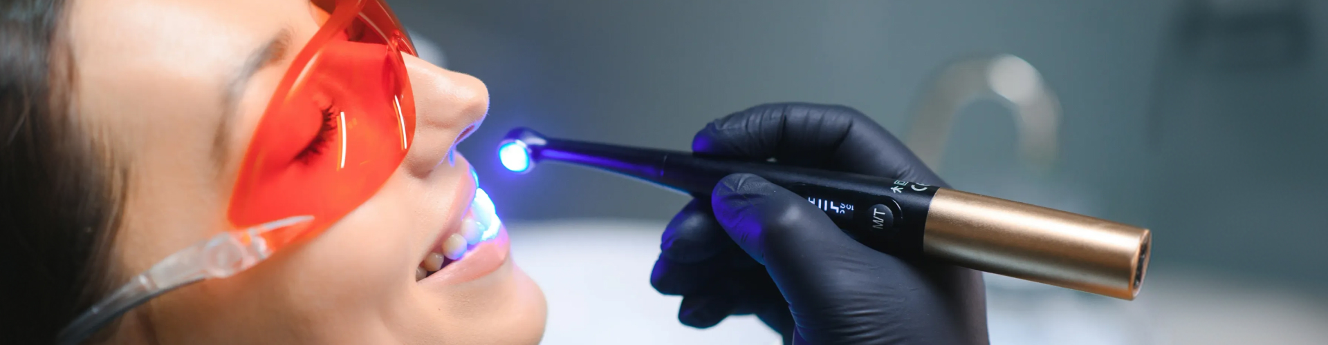 Close-up of a patient wearing protective eyewear during a professional teeth whitening treatment with a dental light.